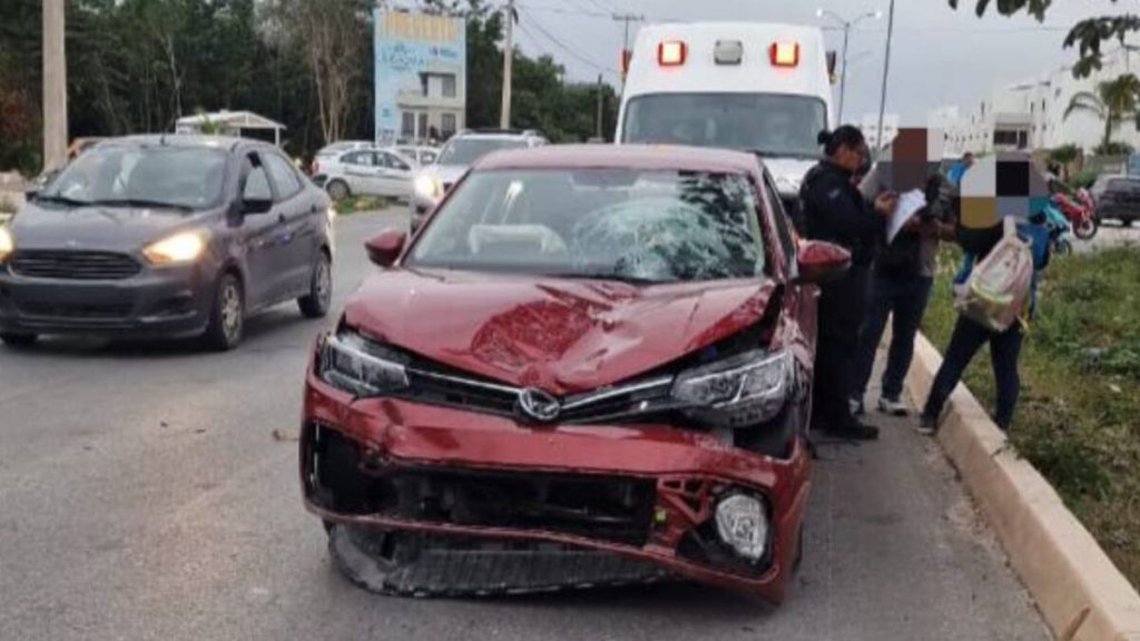 Fotografía del accidente en la Avenida 135 de Cancún, donde se observa un automóvil Volkswagen Virtus rojo y una motocicleta Italika azul, con presencia de elementos de seguridad y peritos en la zona acordonada