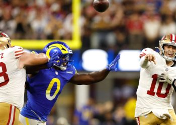 Jugador de los 49ers lanza el balón presionado por la defensa de los Rams en partido de NFL.