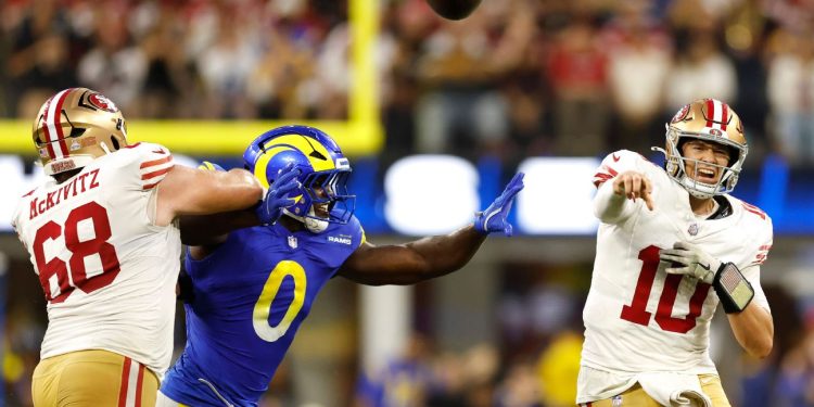 Jugador de los 49ers lanza el balón presionado por la defensa de los Rams en partido de NFL.